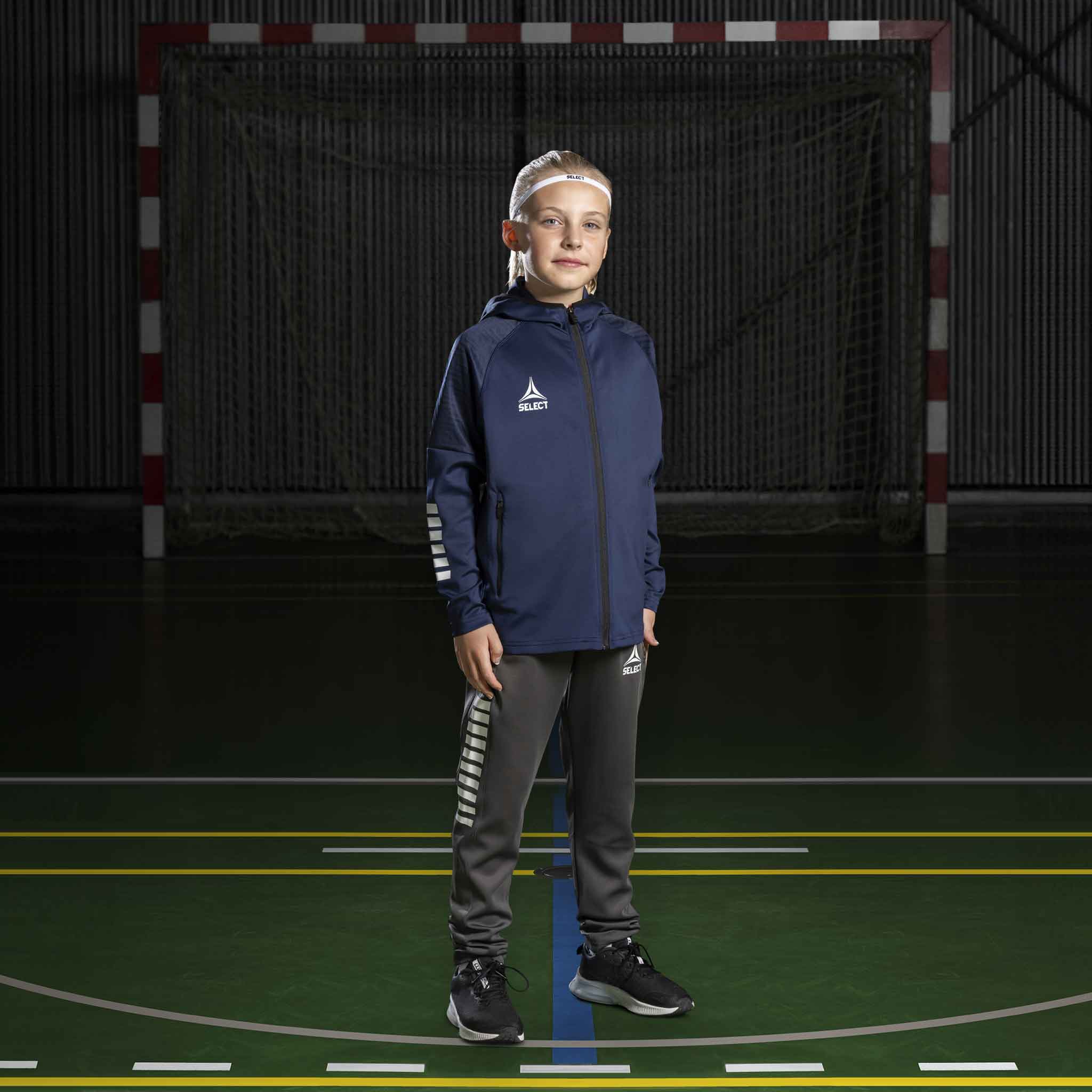 Boy handball player in navy/white Zip hoodie Monaco v24 and grey pants, Match & Training wear, on court.