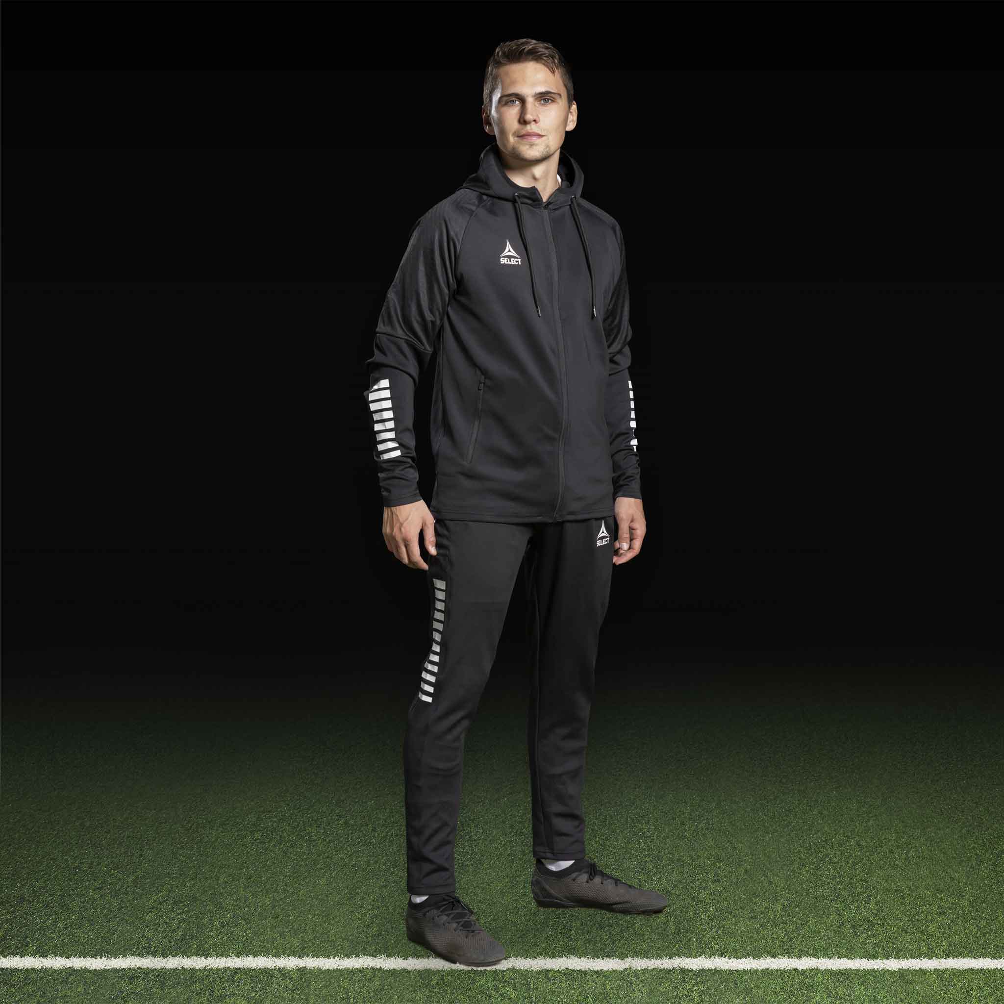 Male football player in black Zip hoodie Monaco v24, Match & Training wear, with white details on sleeves.