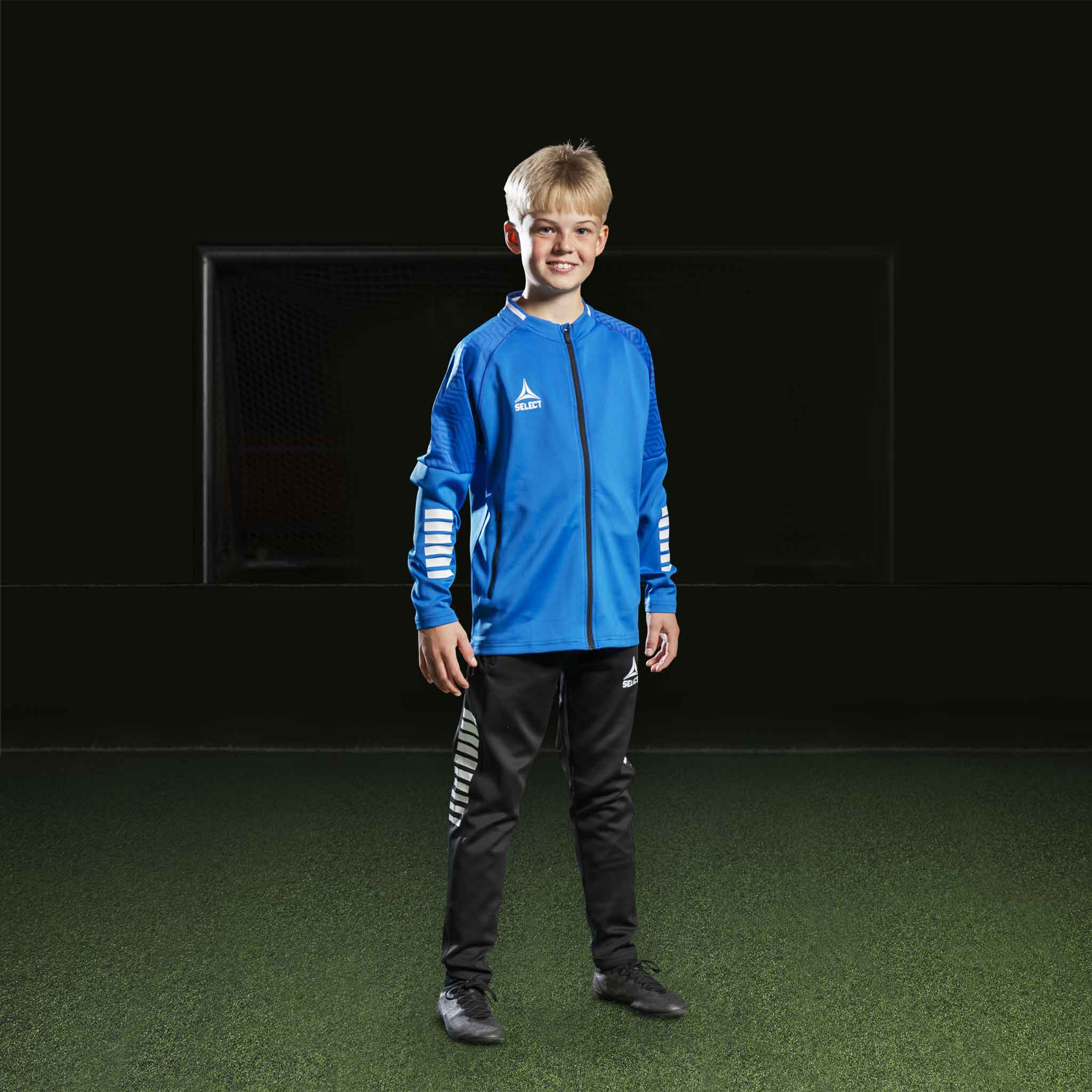 Boy football player in blue/white Zip jacket Monaco v24 and black pants, Match & Training wear, front view.