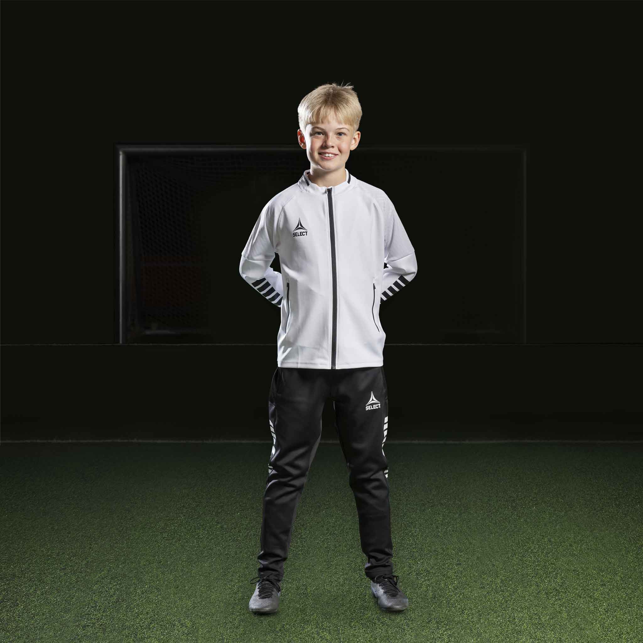 Boy football player in white Zip jacket Monaco v24 and black pants, Match & Training wear, front view.