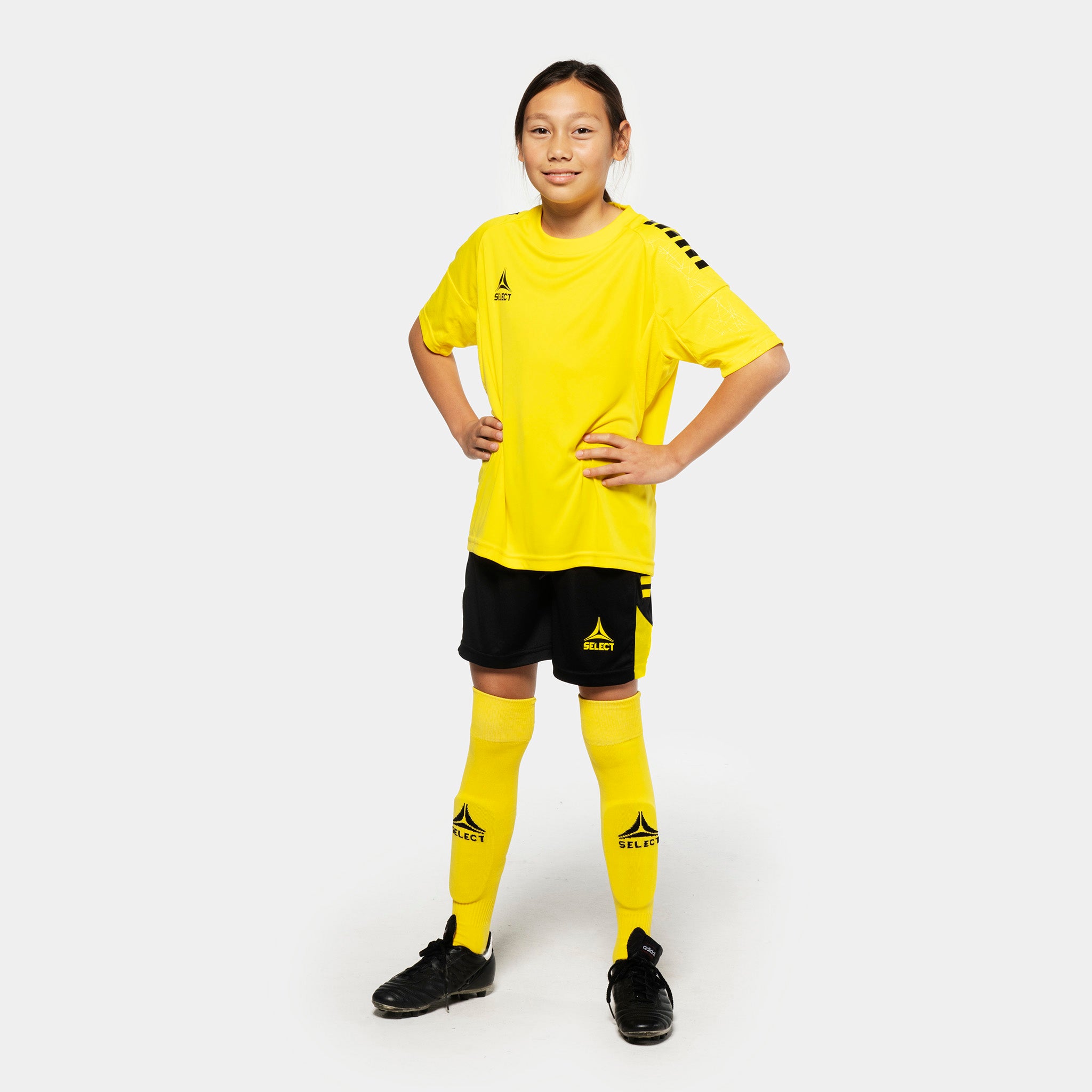Girl football player in yellow shirt, black Player shorts Spain v25 and yellow socks. Match & Training wear, front view.