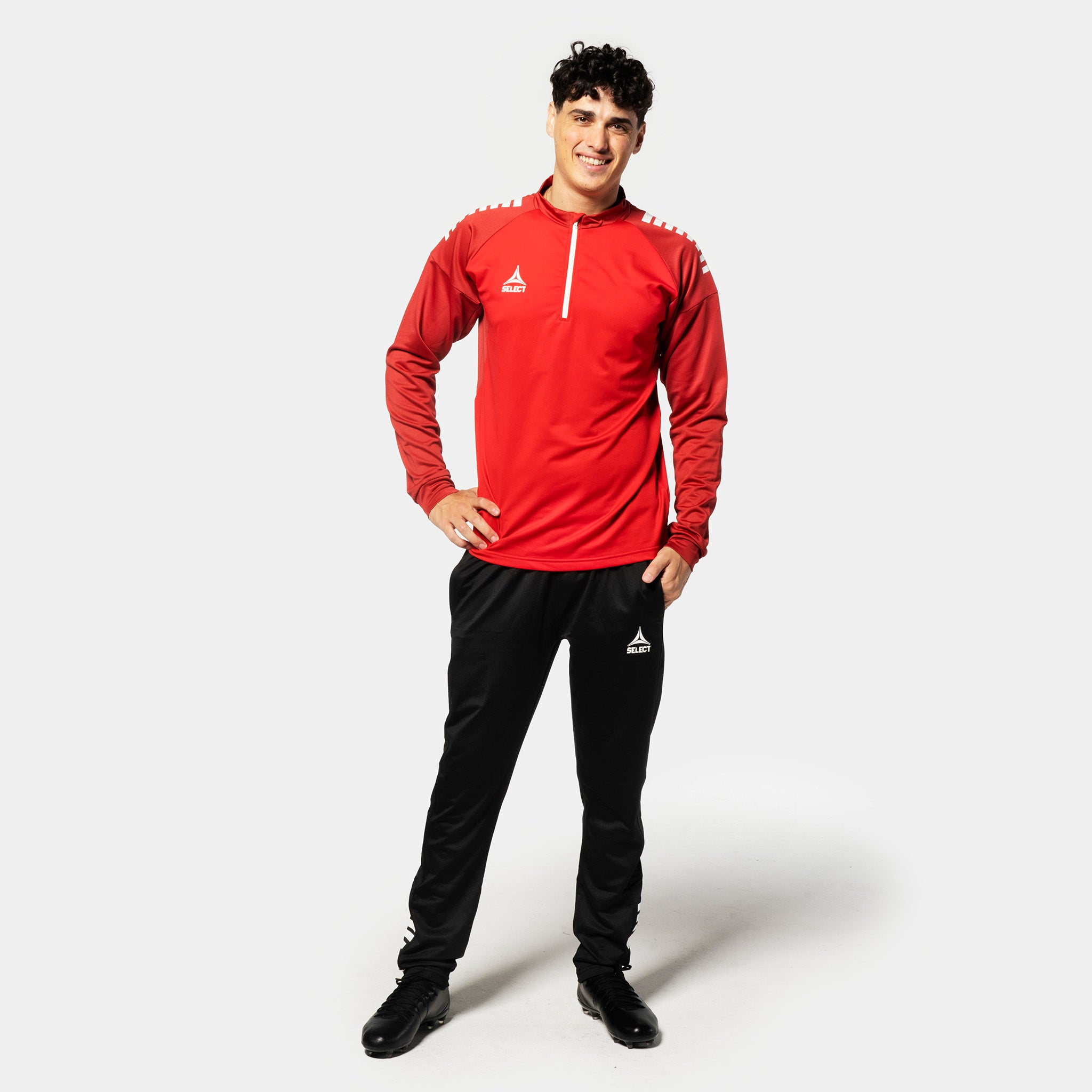 Male football player in red/white Training sweat 1/2 zip Spain v25, Match & Training wear, with black pants, front view