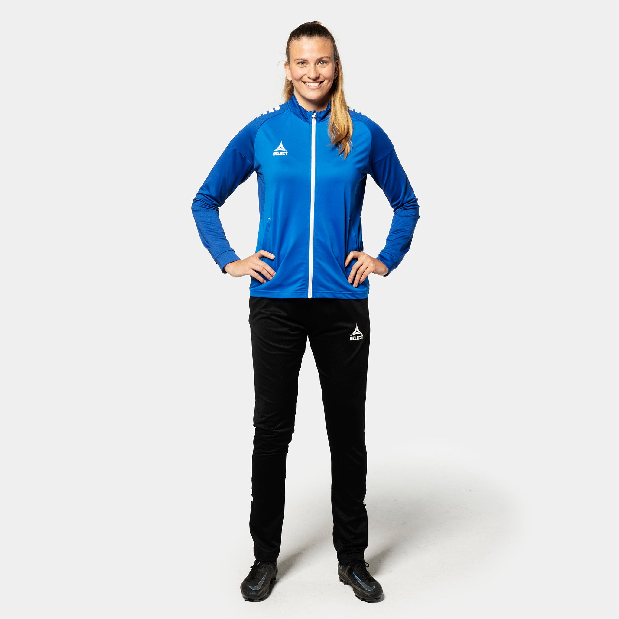 Woman football player in blue-white Training zip jacket Spain woman v25, Match & Training wear, with black pants, front view.