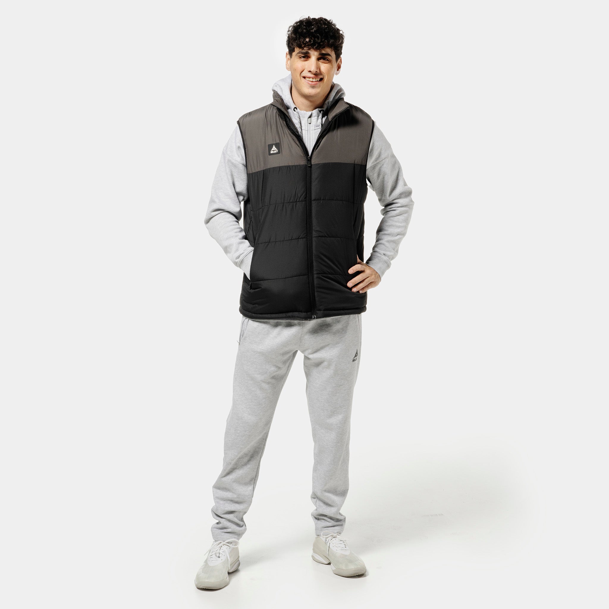 Man in grey Sweat pants Oxford v25 and black padded vest, football leisure wear, front view.