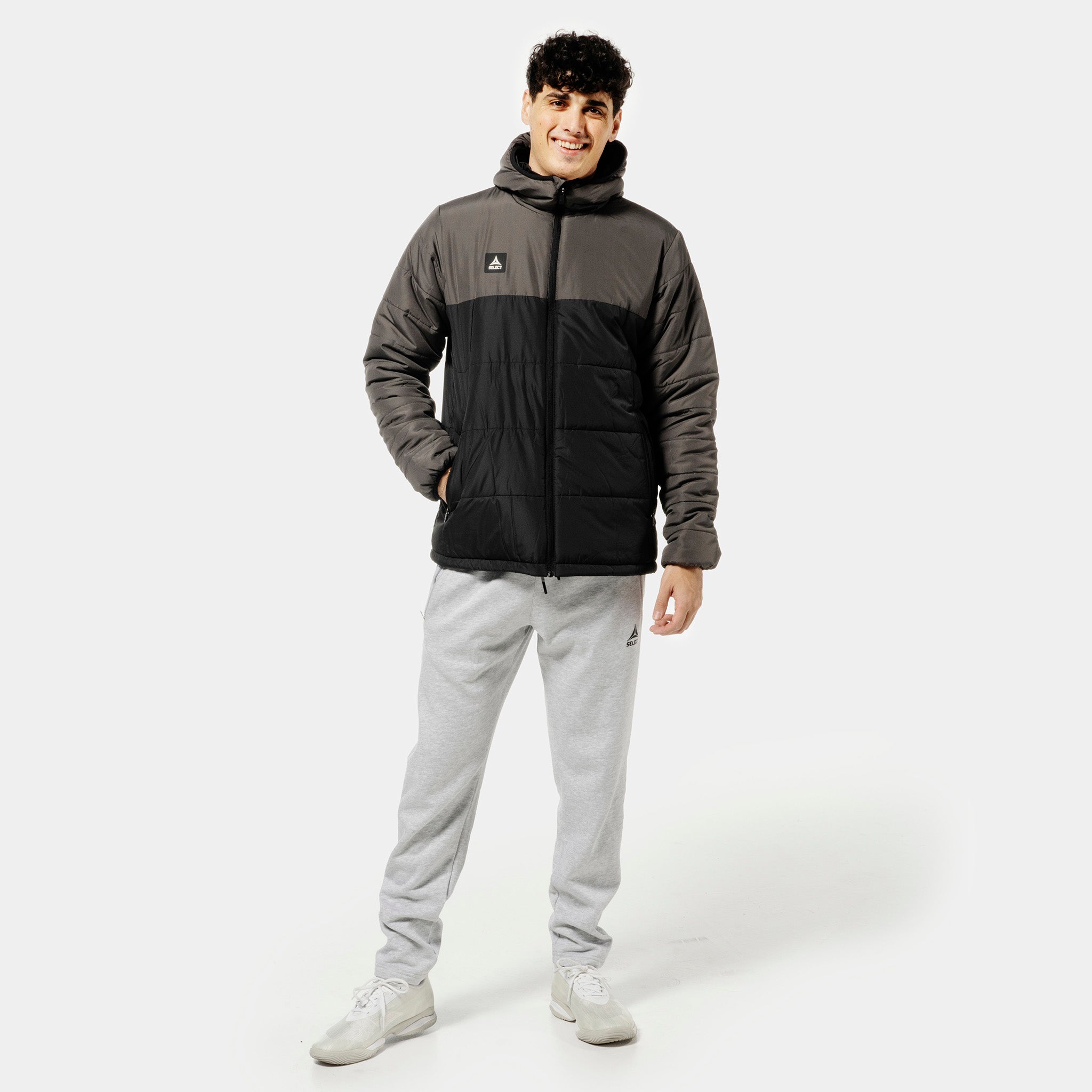 Man footballer in grey Sweat pants Oxford v25 leisure wear, paired with black and grey padded jacket, front view.