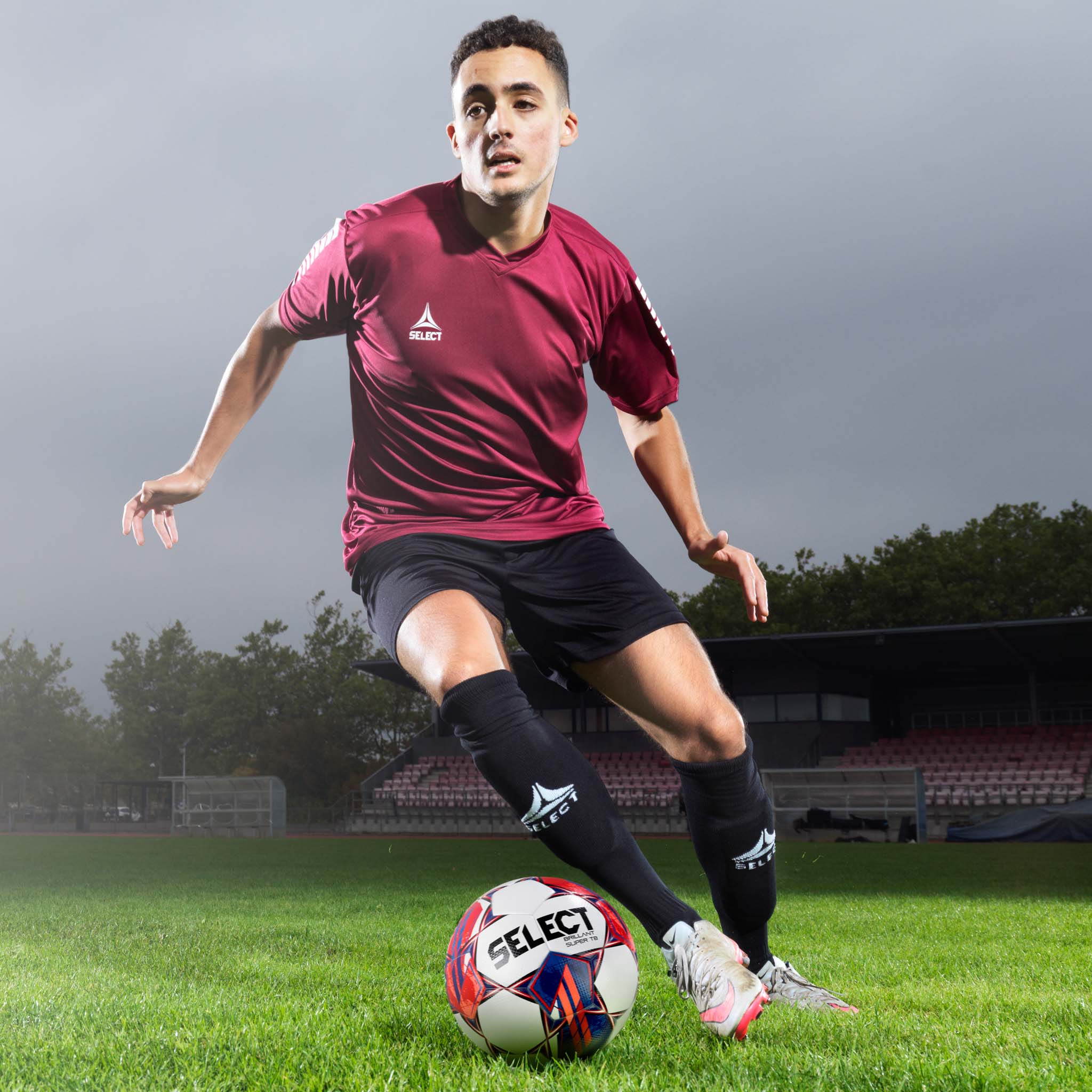 Male football player in action wearing black Pisa Player Shorts, Match & Training wear, with maroon jersey and ball.
