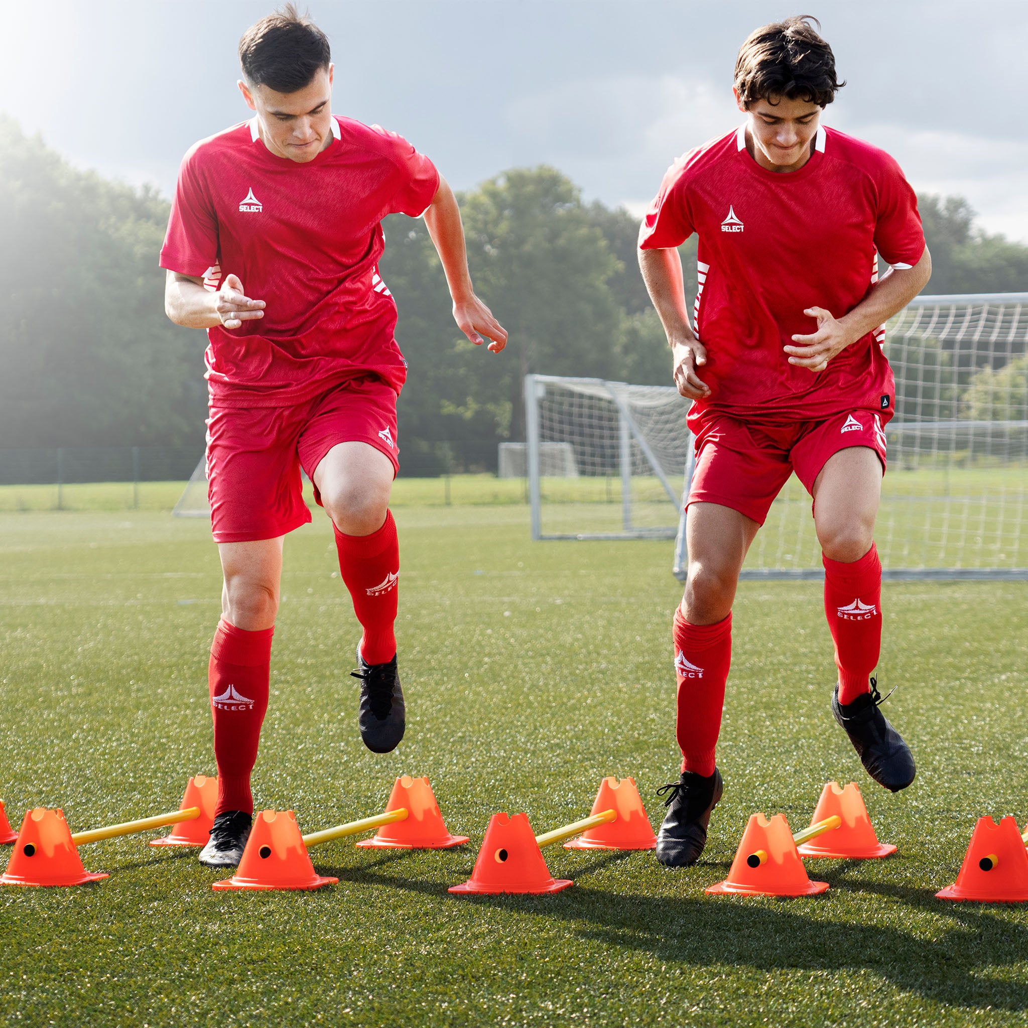 Football players training with orange Agility set w/cones and poles, training equipment, action shot