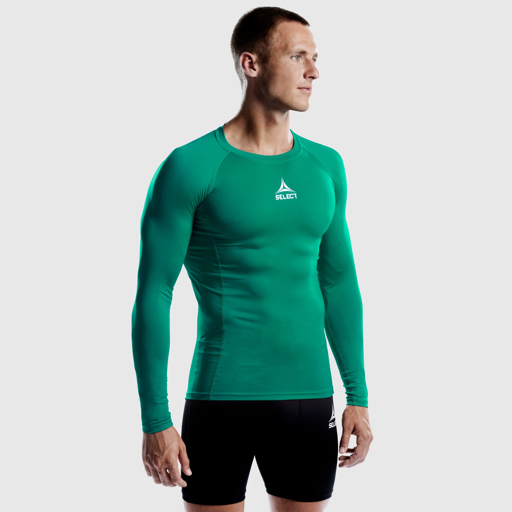 Man football player in green Shirts L/S Baselayer, front view. Baselayer with black shorts and white logo.