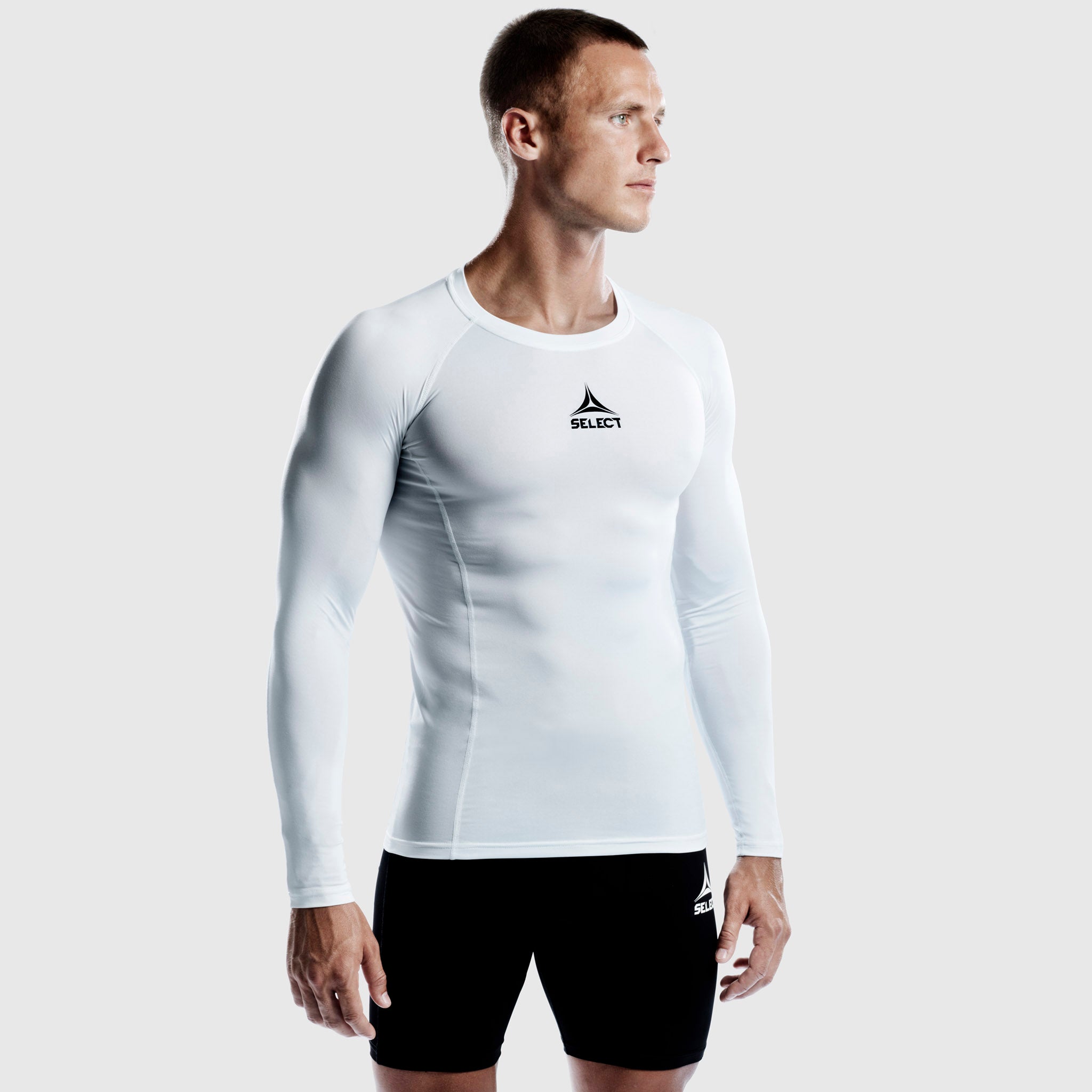 Man in white long-sleeve Shirts L/S Baselayer, a football player wearing the baselayer with black shorts.
