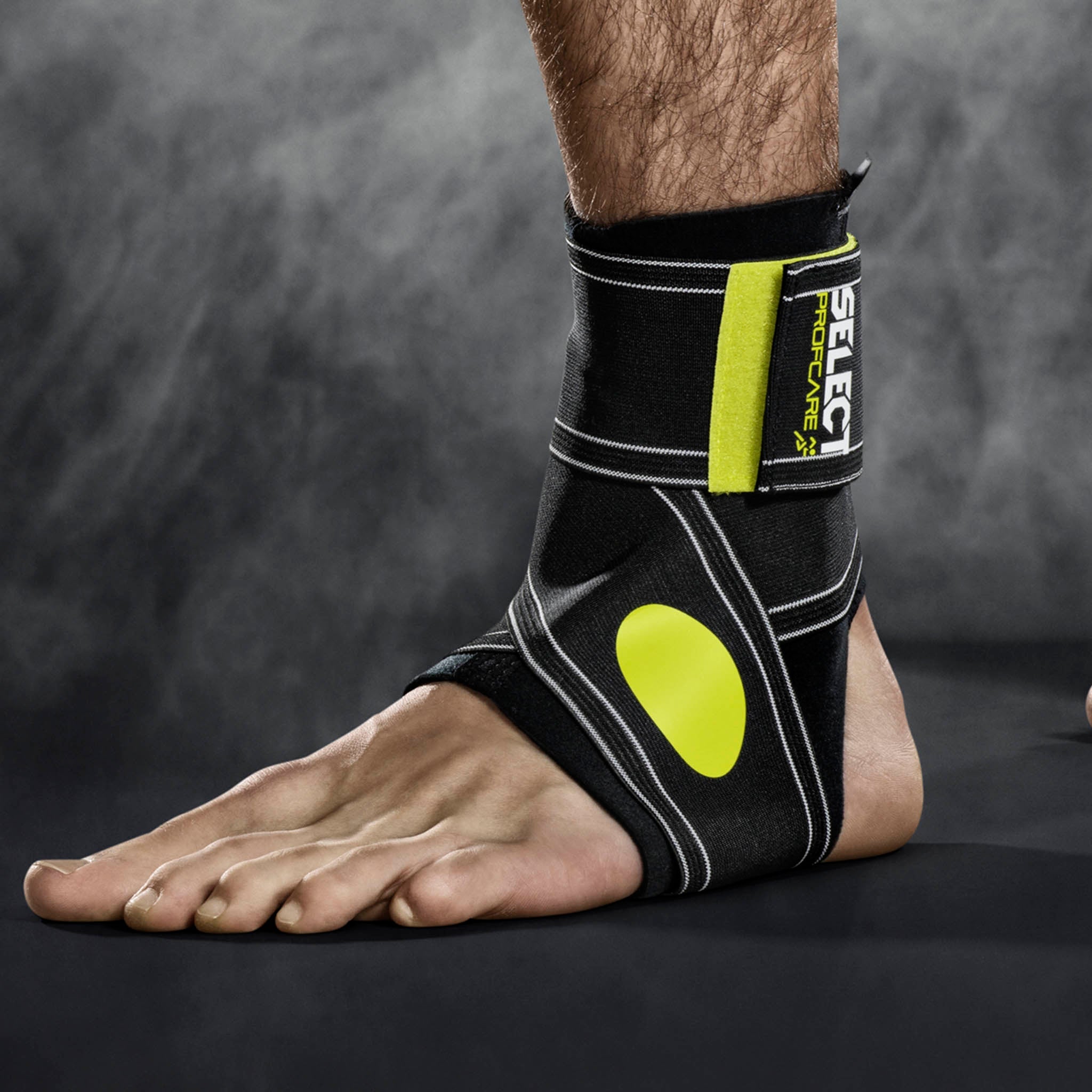Sort og grøn Ankle support 2-parts sportsstøtte på en fod, nærbillede af remme og design.