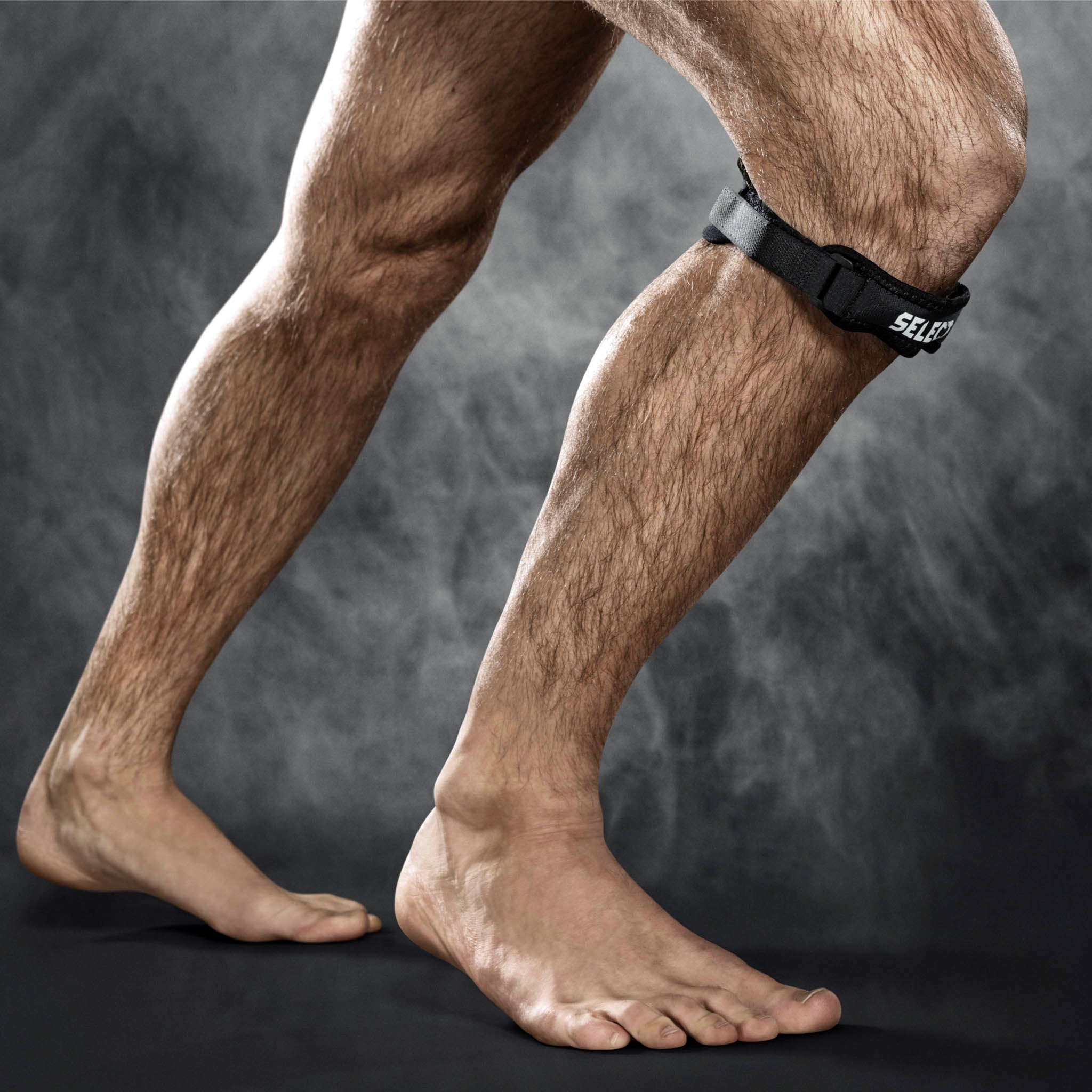 Sort Knee strap sportsstøtte båret af en mandlig fodboldspiller, vist på benet under knæet.