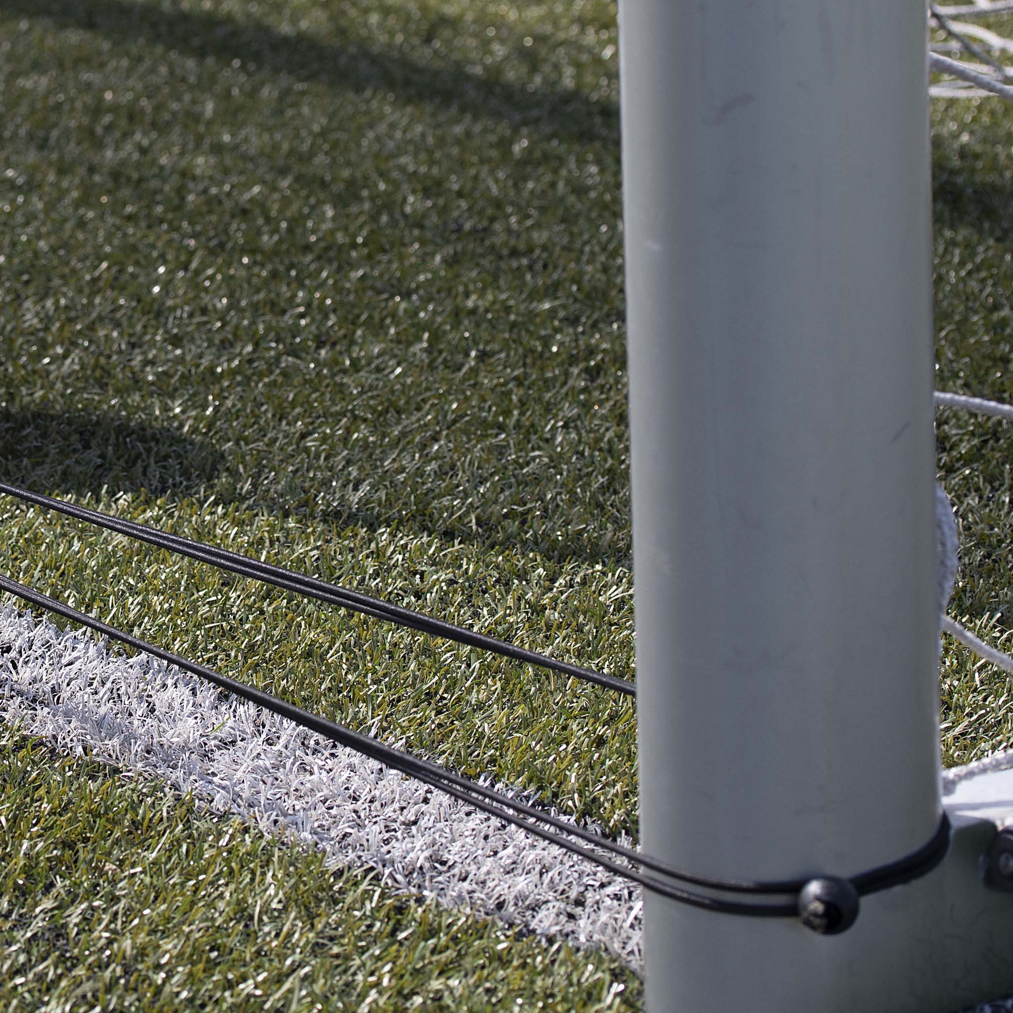 Closeup of black Goal net elastic cord attached to grey post on green football pitch, training equipment.