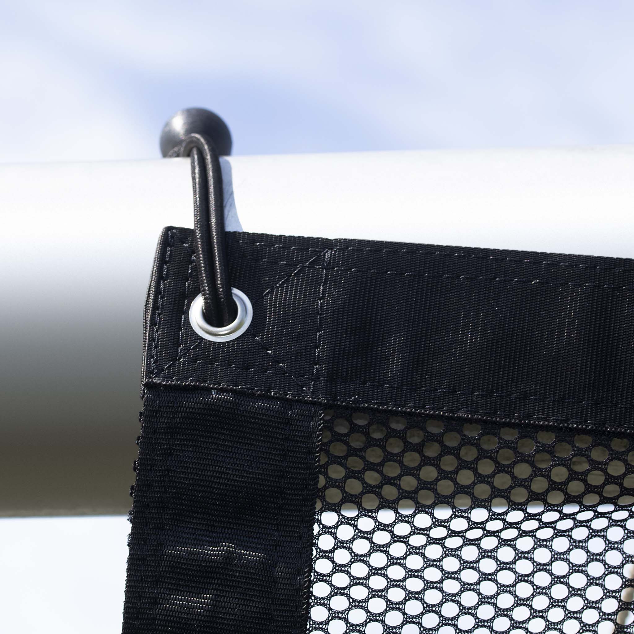 Closeup of black Goal net training equipment, showing elastic hook and metal eyelet on white football goal frame.