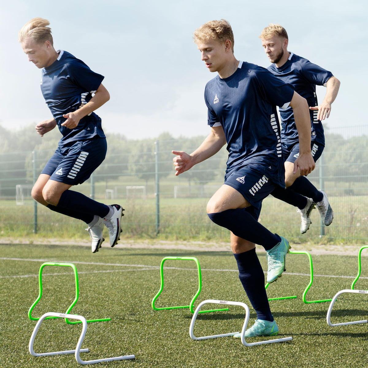 Football players training over green Training hurdles on a field. Training equipment, action shot.