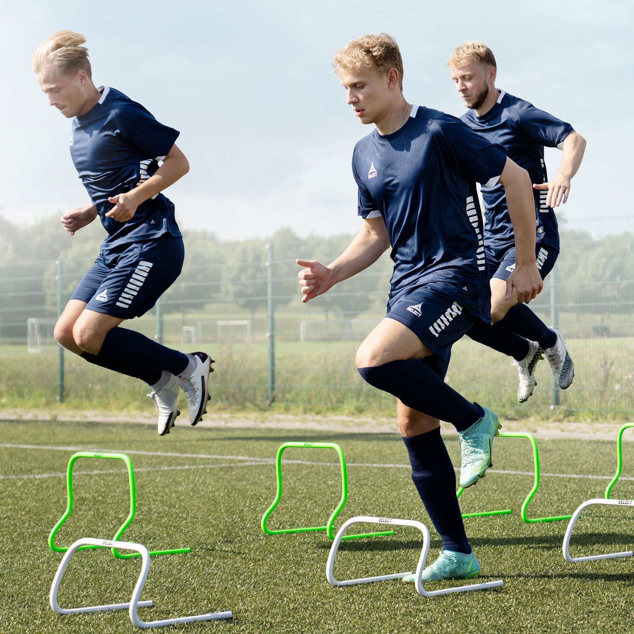 Front page action shot of football players using green Training hurdle training equipment on a field.